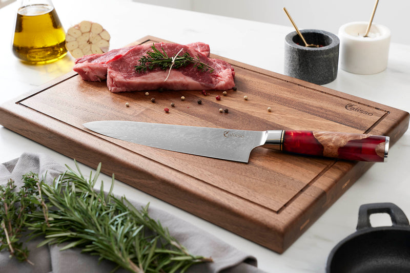 Chefmesser auf dem Walnuss Schneidebrett mit rohem Fleisch und einigen Kräutern und Gewürzen im Hintergrund