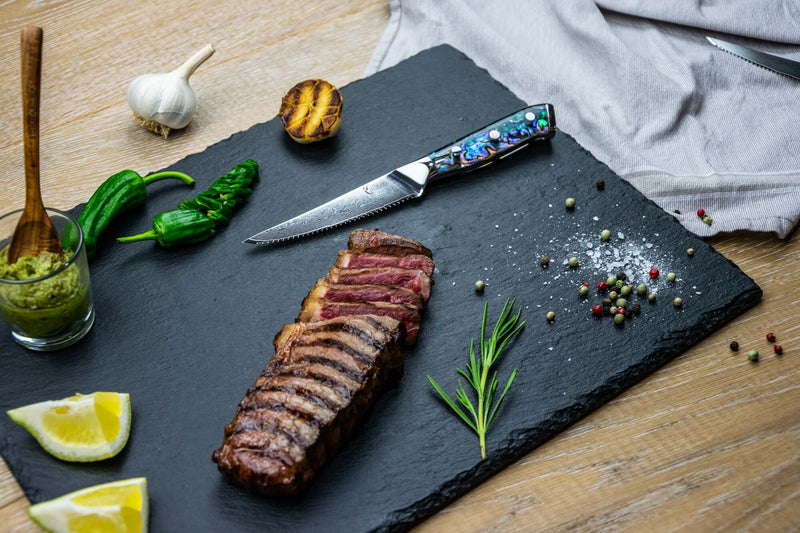 Abalone Steakmesser in einem Servierbrett mit einem Steak, Kräutern und Gewürzen.